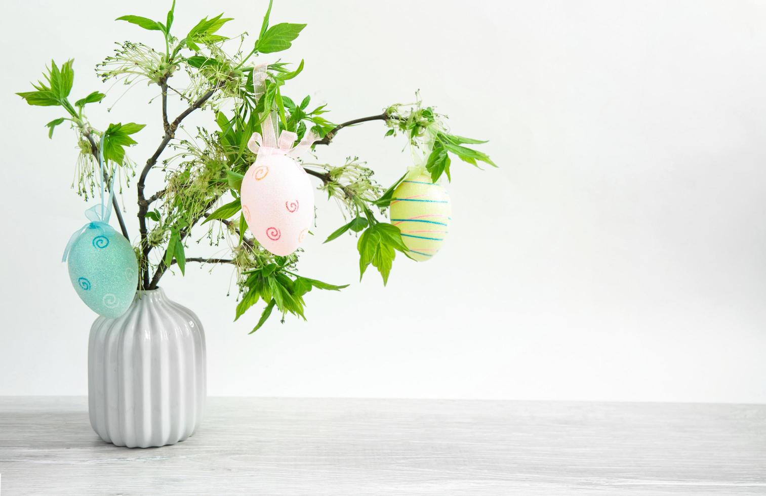 um buquê de galhos verdes com folhas frescas florescendo em um vaso em cima da mesa é decorado com ovos de páscoa coloridos. decoração no interior da casa para a páscoa. espaço de cópia foto