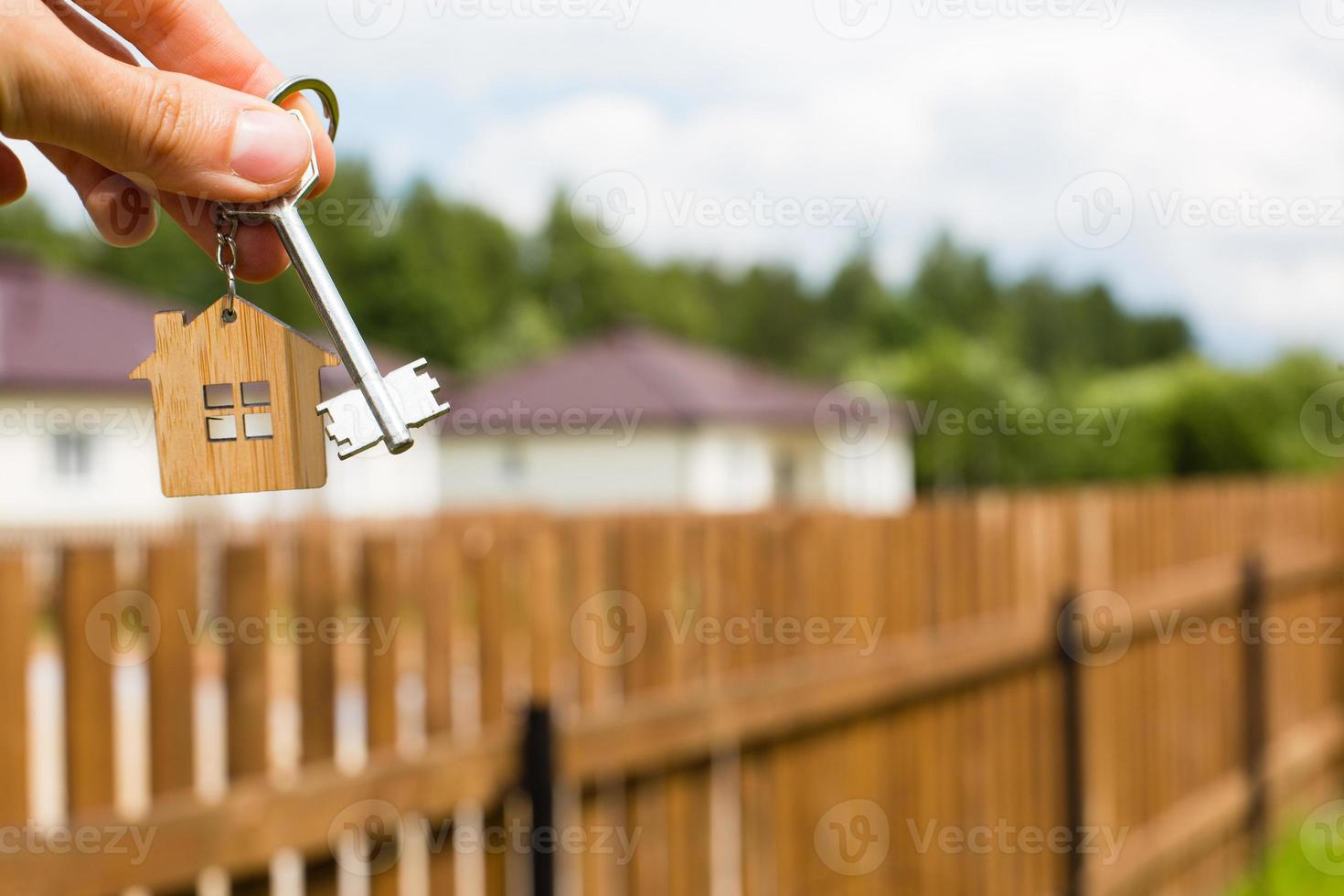 pingente de madeira de uma casa e chave. fundo de cerca e casa de campo. sonho da casa, construção, projeto, entrega do projeto, mudança de casa, hipoteca, aluguel e compra de imóveis. espaço de cópia foto