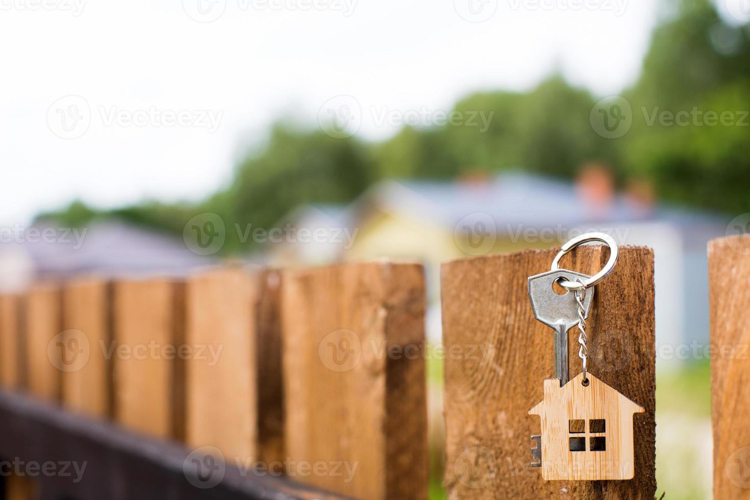 pingente de madeira de uma casa e chave. fundo de cerca e casa de campo. sonho da casa, construção, projeto, entrega do projeto, mudança de casa, hipoteca, aluguel e compra de imóveis. espaço de cópia foto