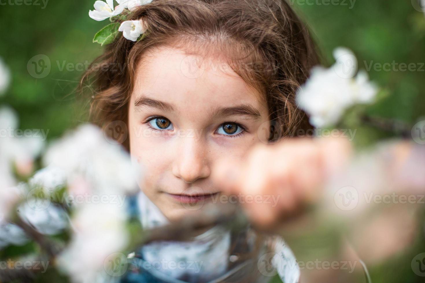 uma menina bonitinha de 5 anos em um pomar de maçãs brancas florescendo na primavera. primavera, pomar, floração, alergia, fragrância primaveril, ternura, cuidado com a natureza. retrato foto