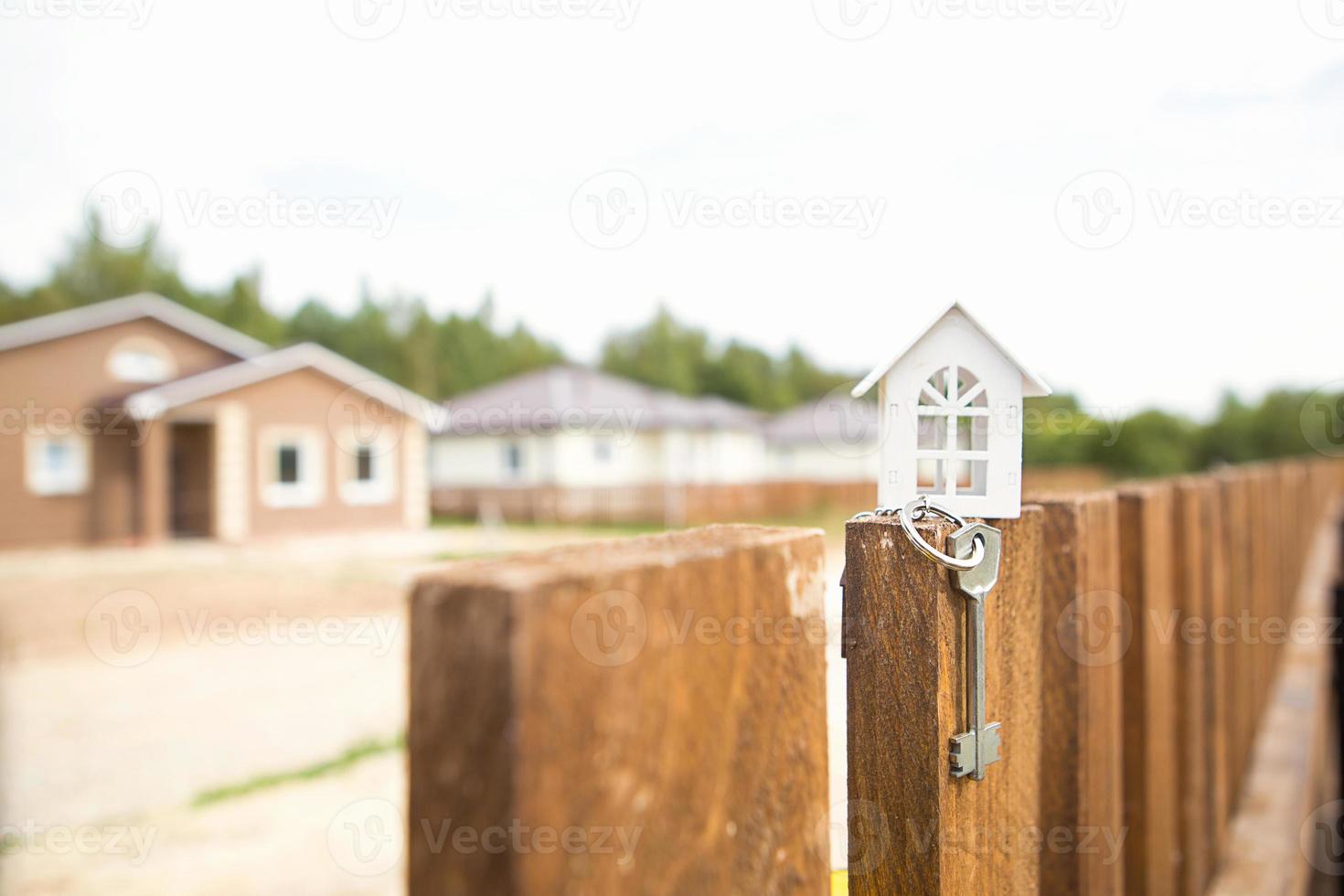 pequena figura de casa de madeira branca na cerca com chave para habitação no contexto das casas de campo. construir, projetar, projetar, mudar de casa, hipotecar, alugar e comprar imóveis. espaço de cópia foto