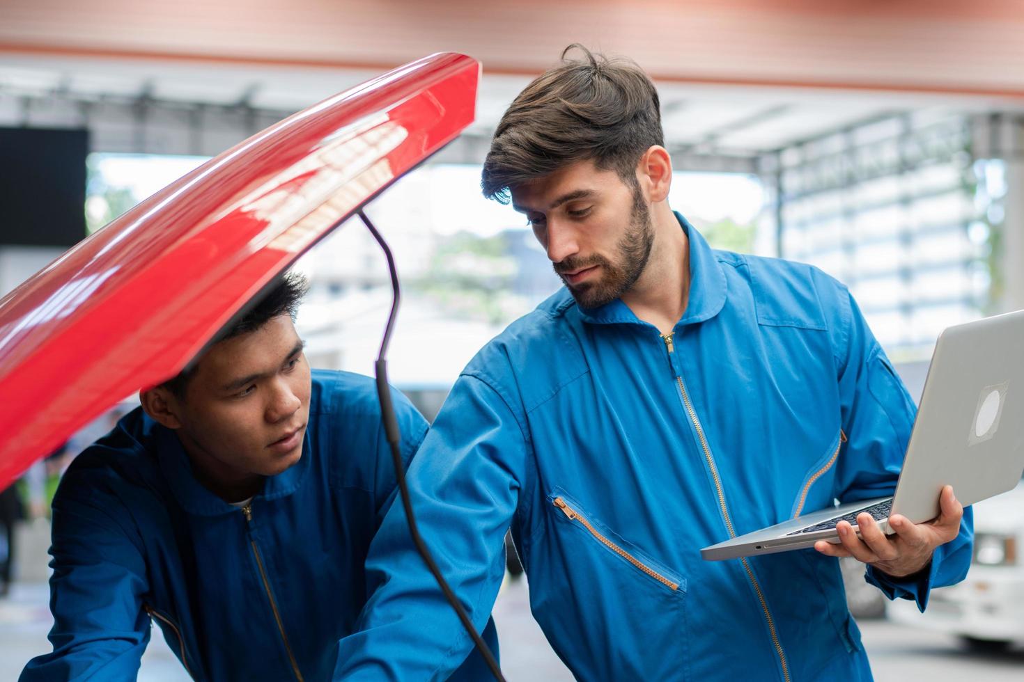 homem mecânico de automóveis caucasiano usando computador portátil diagnóstico e reparação de carro enquanto seu colega verificando o capô do radiador na garagem automotiva, manutenção do técnico de motores após o serviço foto