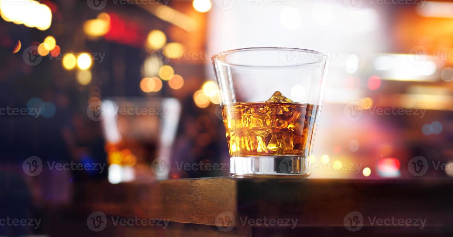 copo de bebida de uísque com cubo de gelo no fundo da barra de madeira de mesa foto