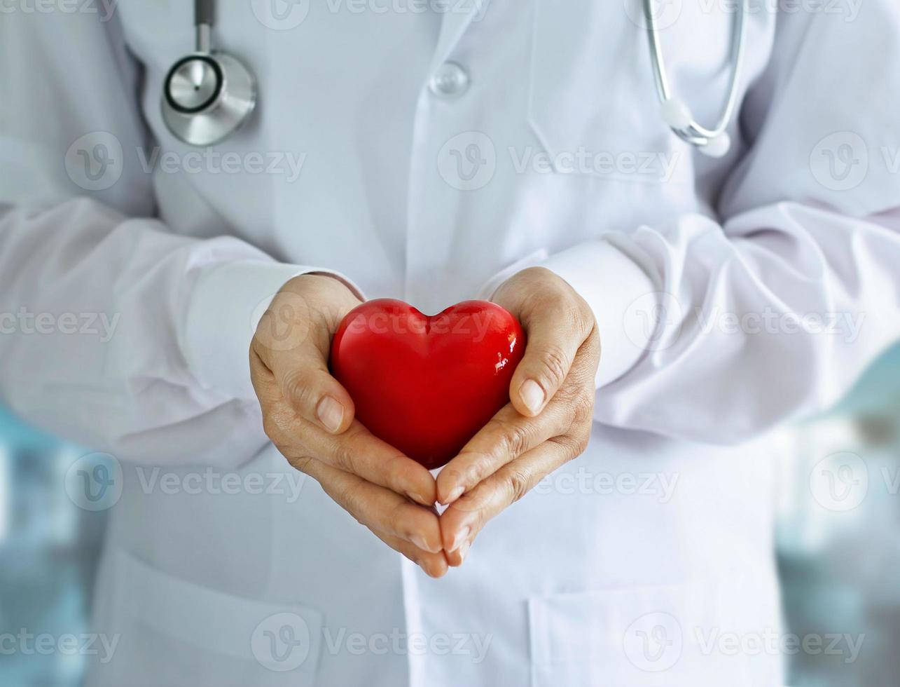 médico com estetoscópio e forma de coração vermelho nas mãos no fundo do hospital foto