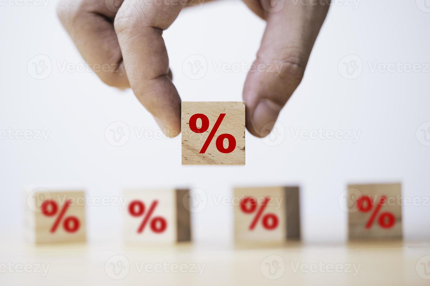mão segurando o símbolo de porcentagem vermelho que imprime a tela no bloco de cubo de madeira para taxa de juros da dívida e conceito de desconto de compras. foto