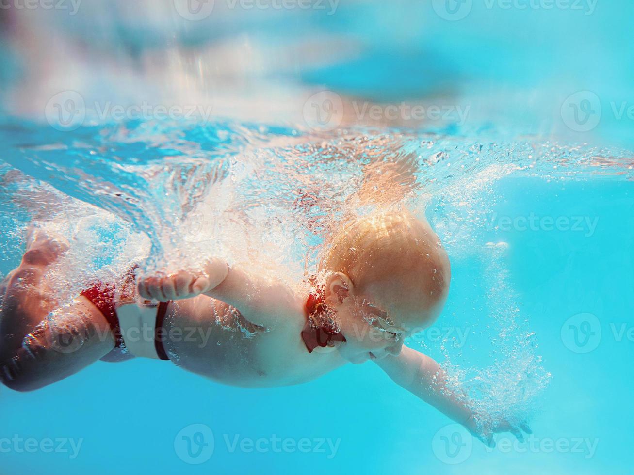 menino infantil com borboleta vermelha mergulhando debaixo d'água na piscina, aprenda a nadar. conceito de esporte e férias foto