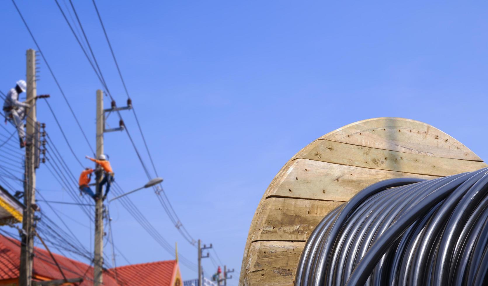 bobina de madeira de cabo elétrico com fundo desfocado do grupo de eletricistas trabalhando em postes de energia contra o céu azul foto