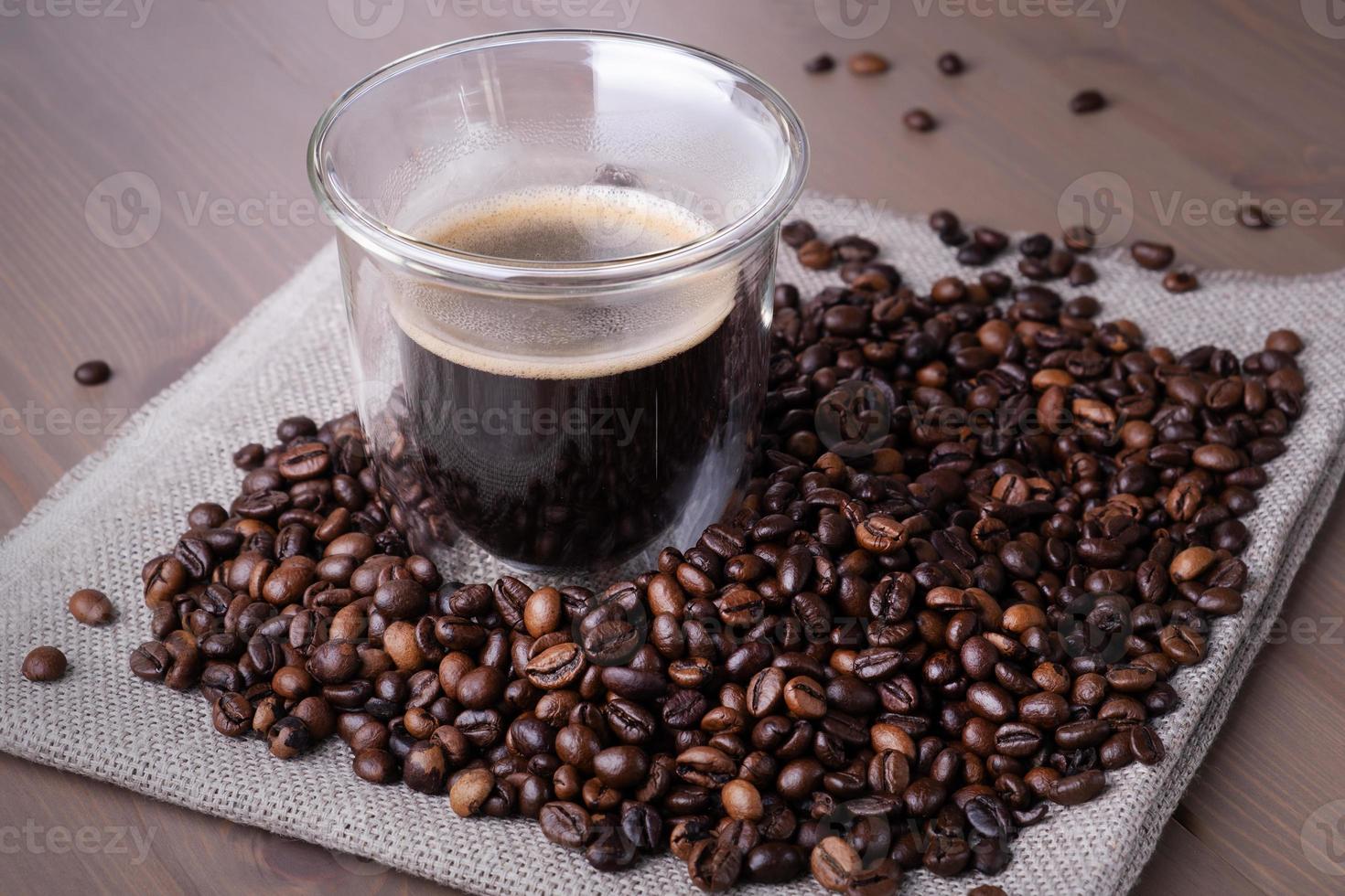 copo de vidro com café e pilha de grãos de café torrados foto