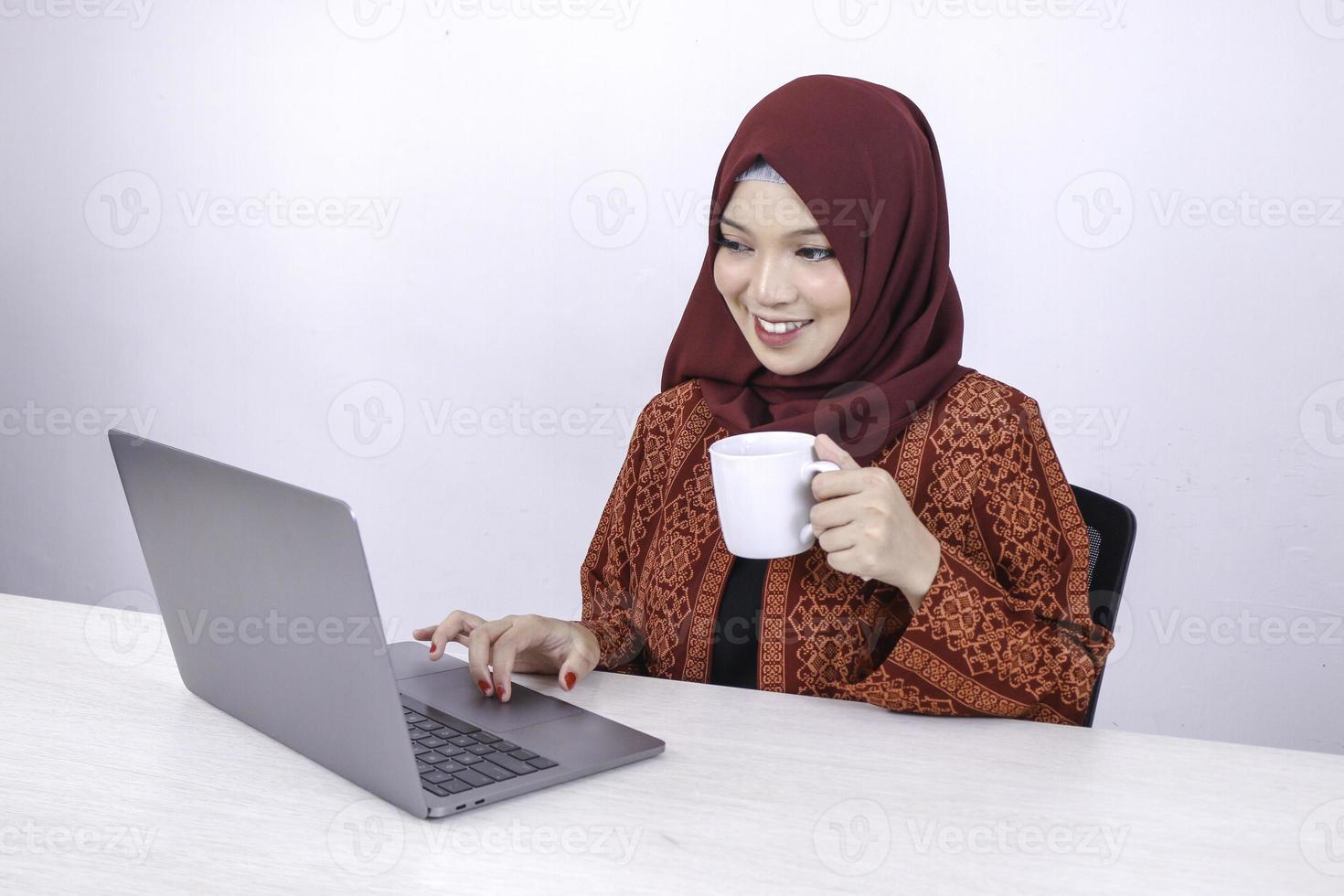 bela jovem islâmica asiática gosta de trabalhar no computador portátil enquanto está sentado na sala branca, bebendo café. foto