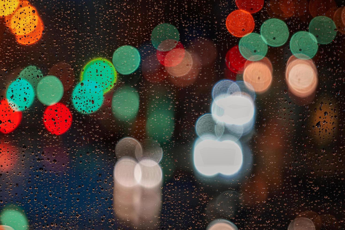 gotas de chuva na janela e luzes da rua à noite na cidade foto