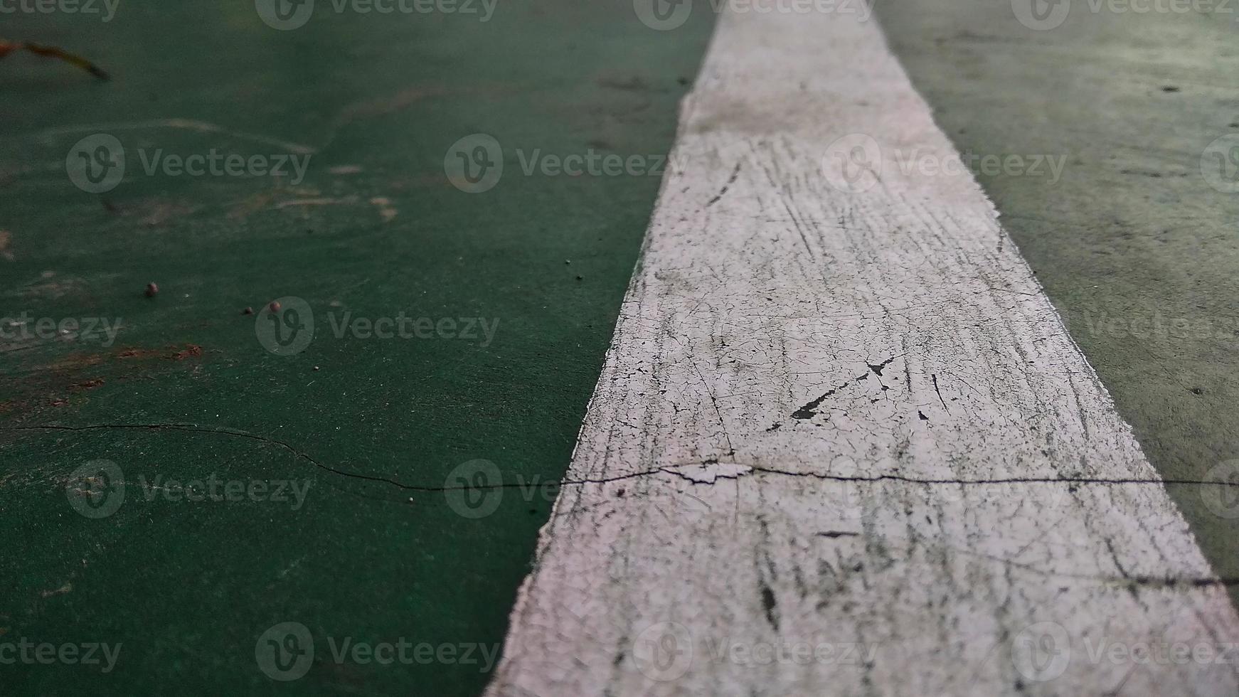 close-up de uma linha branca rachada desenhada em um piso quebrado em verde no campo de esportes público. foto