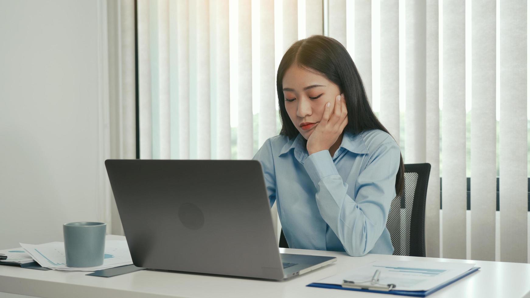 jovens mulheres asiáticas estão entediadas no trabalho e sentem preguiça de lidar com dados em seu laptop à tarde. foto