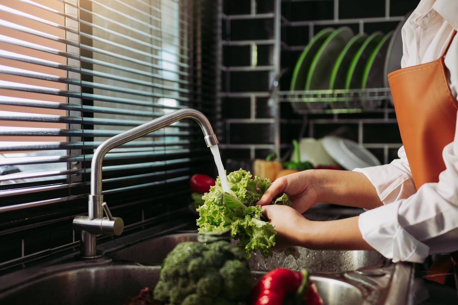 mulher de mãos asiáticas lavando salada de legumes e preparação de alimentos saudáveis na cozinha. foto