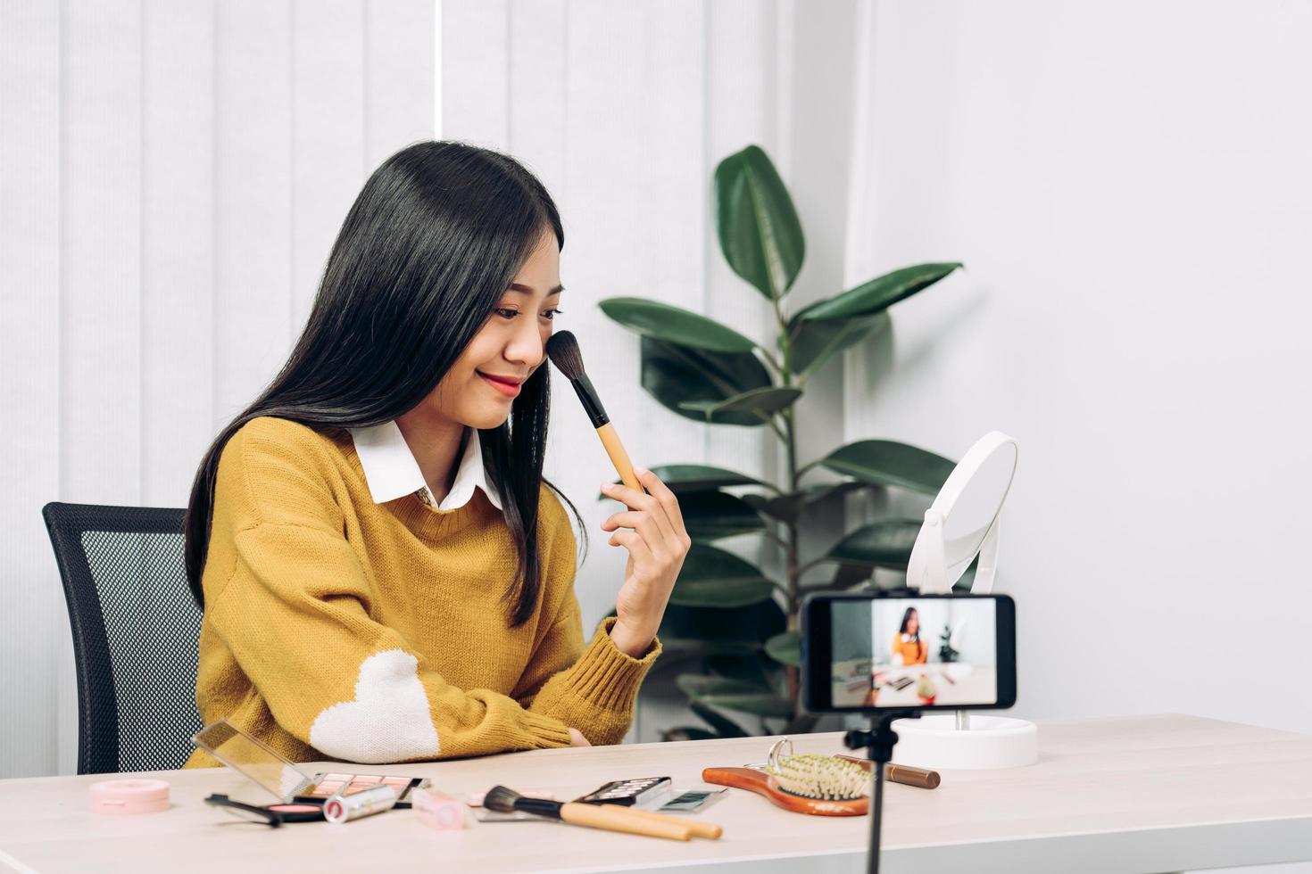 jovem mulher asiática vlogging sobre produtos cosméticos para cuidados com a pele na mesa com sua câmera de vídeo e demonstra o uso do produto e comentários para seu canal de blog online. foto