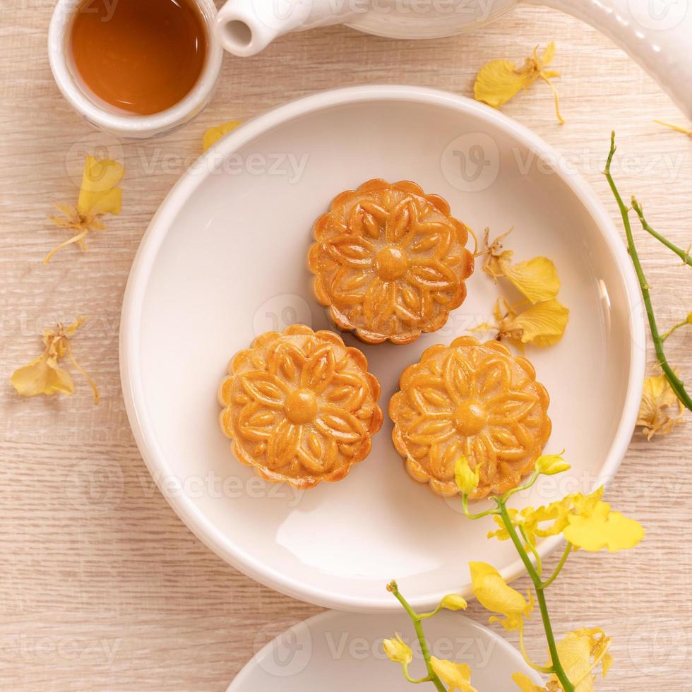 delicioso bolo de lua para o festival do meio do outono com belo padrão, decorado com flores amarelas e chá. conceito de design de pastelaria de tarde festiva foto