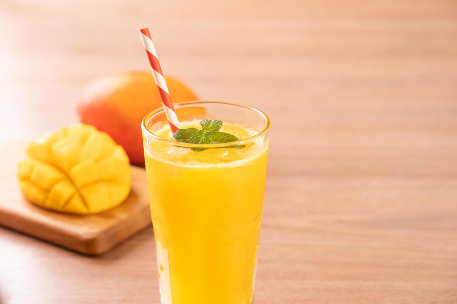 suco de manga fresca com carne de polpa picada linda e palha no fundo da mesa de madeira brilhante. conceito de design de frutas tropicais. feche, copie o espaço. foto