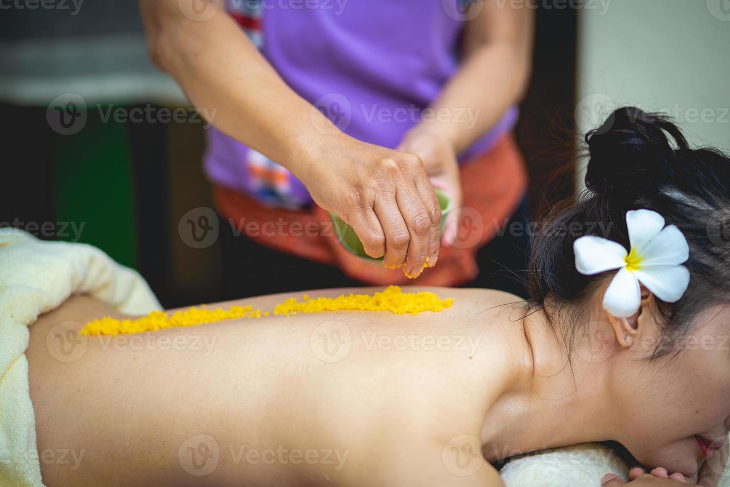 linda mulher desfrutando de uma massagem de esfoliação com sal e tendo tratamento de esfoliação na sala de spa. morena recebendo um tratamento de beleza de esfoliação com sal no spa. esfoliação corporal. foto