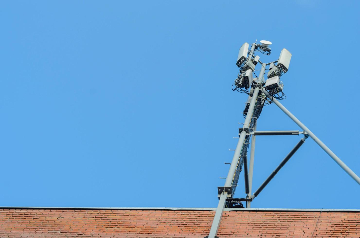 antena celular no telhado de uma casa de tijolos no fundo do céu azul, espaço para texto. foto