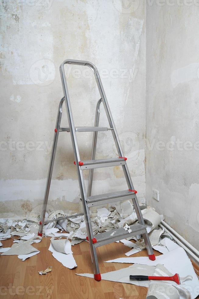 quarto vazio com escada de paredes nuas e restos de papel de parede antigos no chão durante a redecoração foto