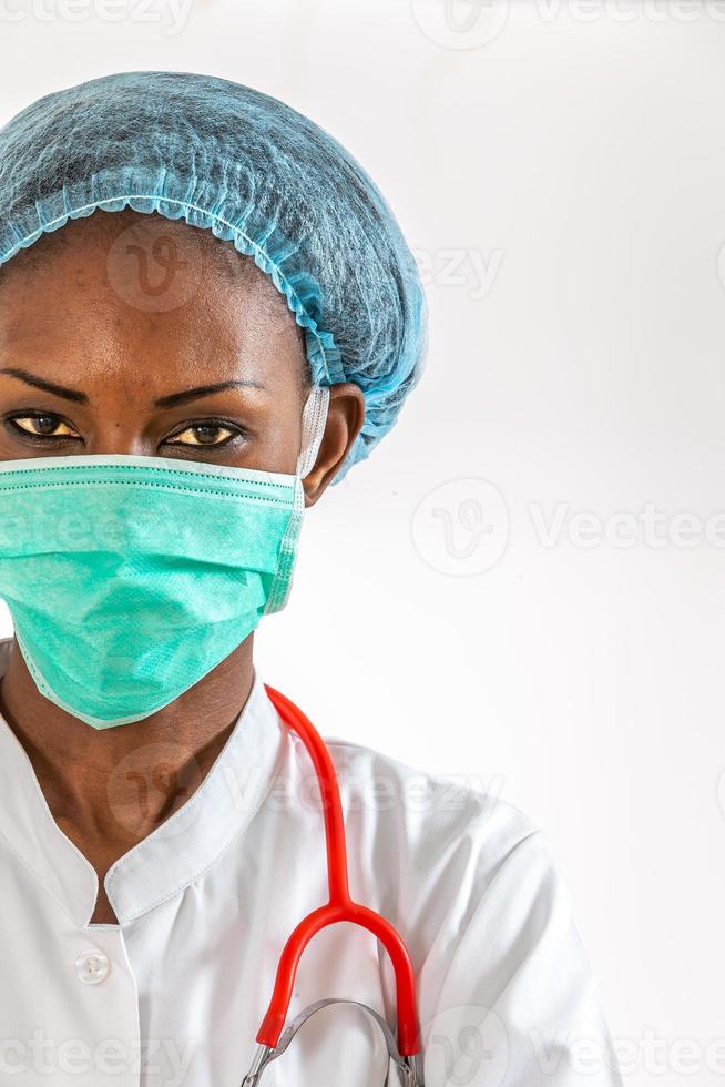 médica africana americana, enfermeira mulher vestindo jaleco, boné, com estetoscópio e máscara. foto