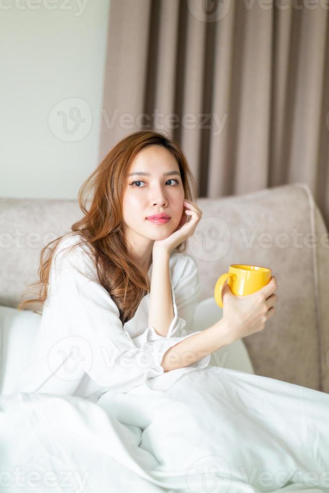 retrato de mulher bonita acordar e segurando uma xícara de café ou caneca na cama foto