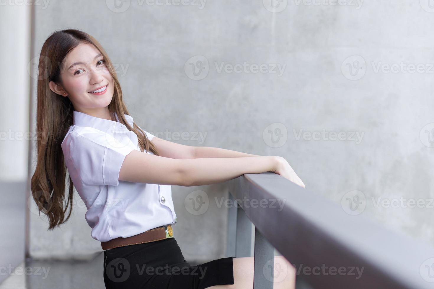 retrato de uma estudante tailandesa adulta em uniforme de estudante universitário. menina bonita asiática sentada sorrindo alegremente na universidade foto