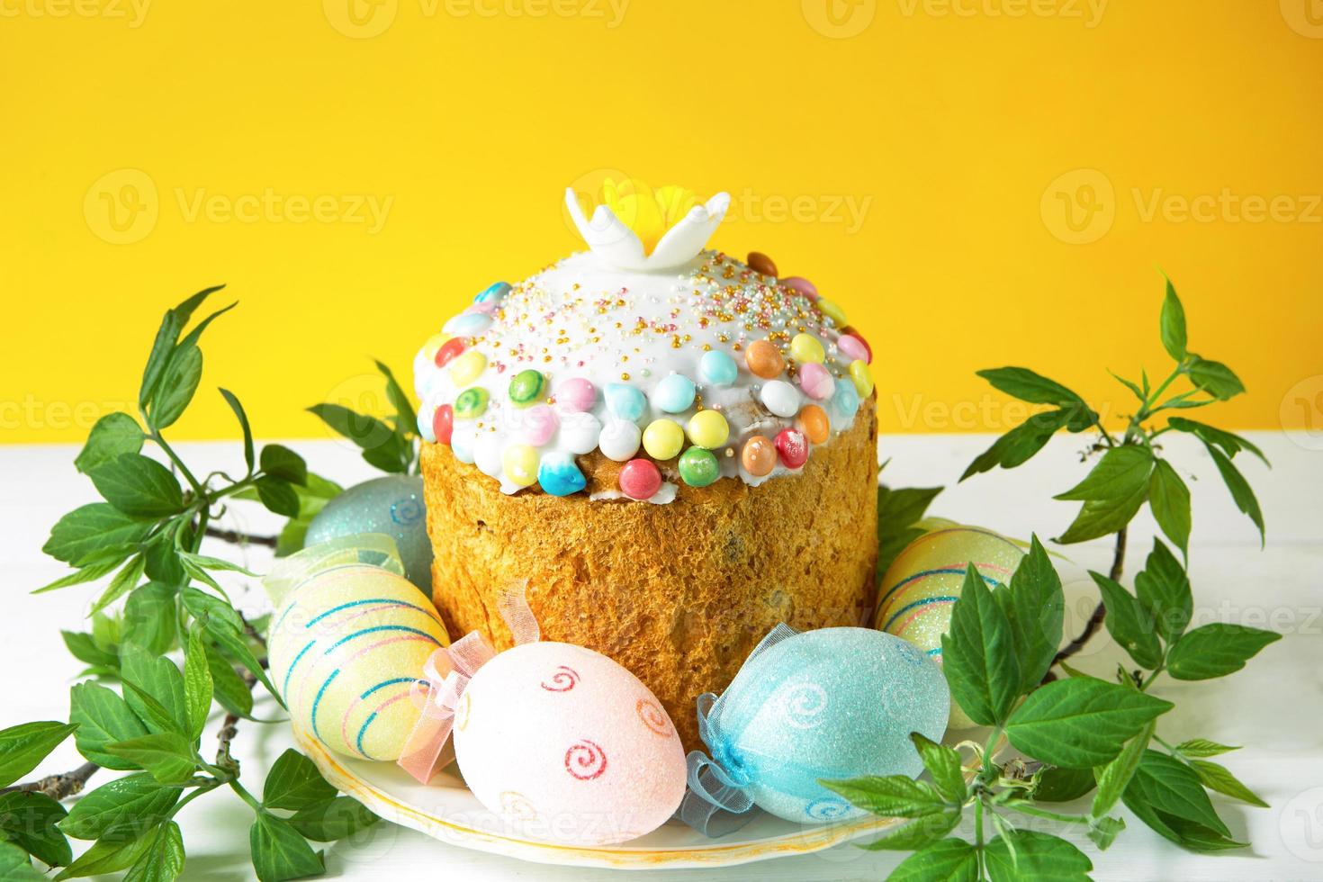 bolo de páscoa com ovos pintados em uma travessa em uma mesa branca. comida festiva tradicional. fundo amarelo foto