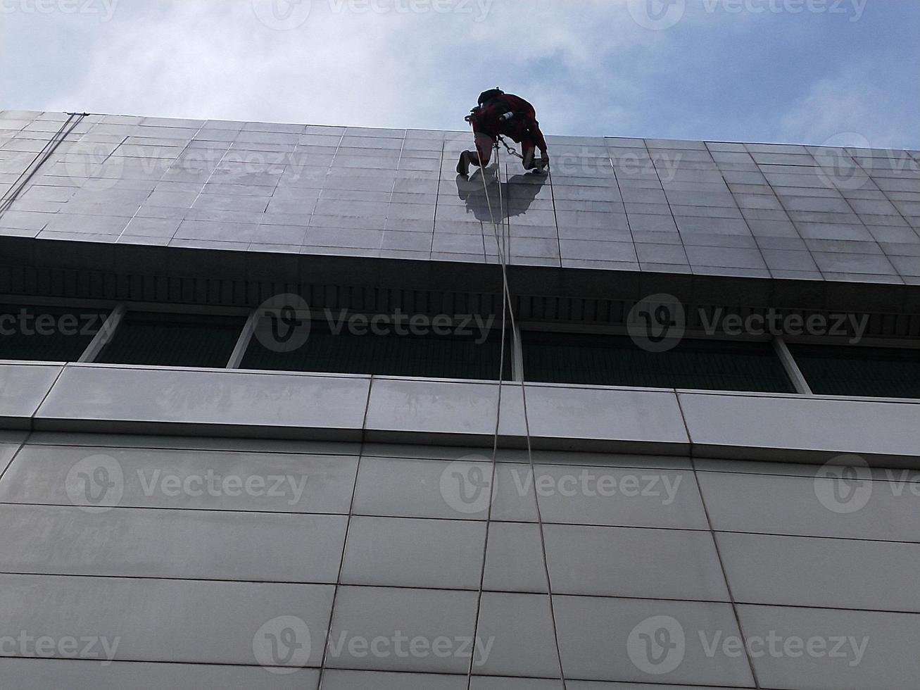 foto de um trabalhador limpando a parte externa do prédio, pendurado em uma corda de segurança