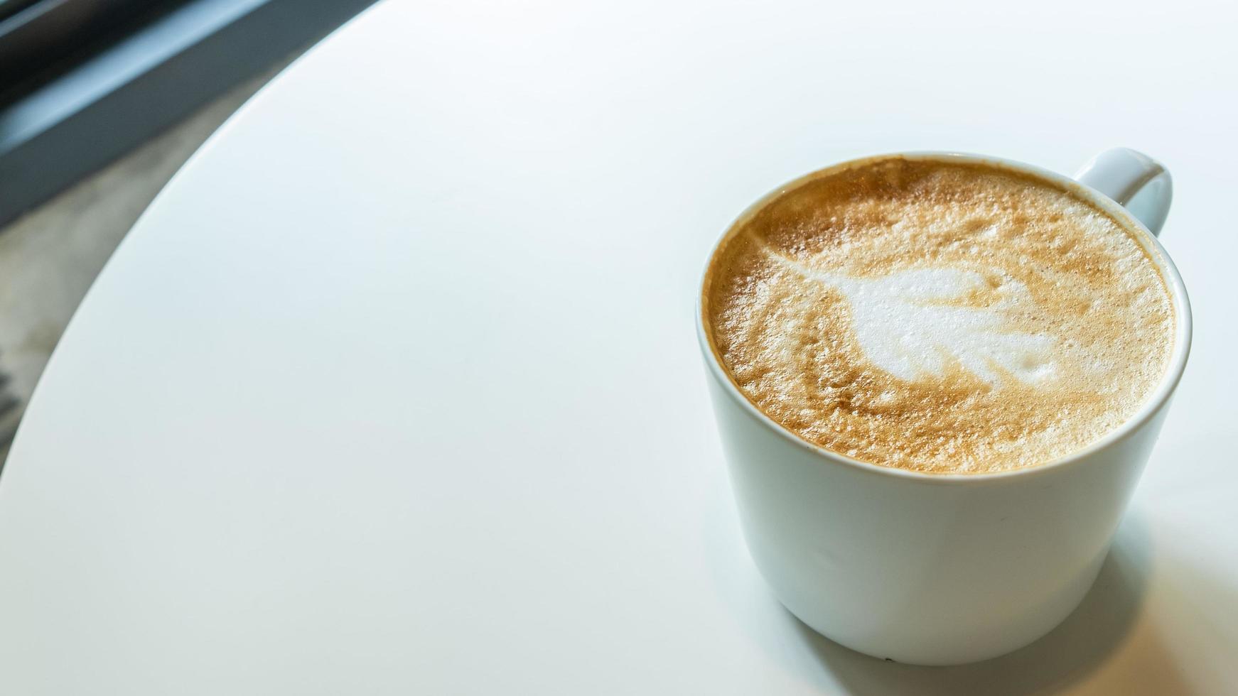 xícara de café com leite e forma de arte no fundo da mesa branca. foto