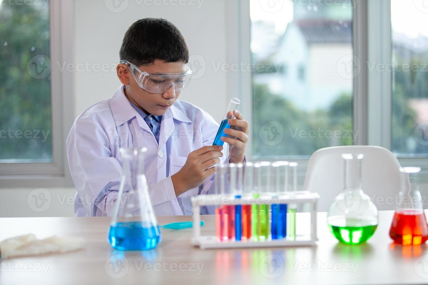 menino mistura produtos químicos em copos. crianças com tubo de ensaio fazendo experimento no laboratório da escola. foto