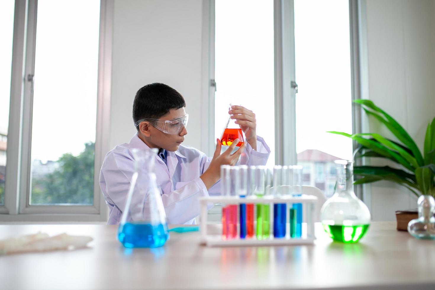 menino mistura produtos químicos em copos. crianças com tubo de ensaio fazendo experimento no laboratório da escola. foto