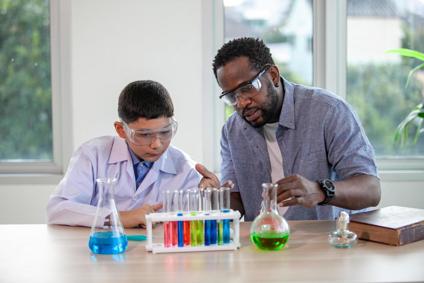 menino mistura produtos químicos em copos. professor entusiasmado explica química para crianças, estudante de química mostrando um novo experimento para a aula de ciências do professor foto