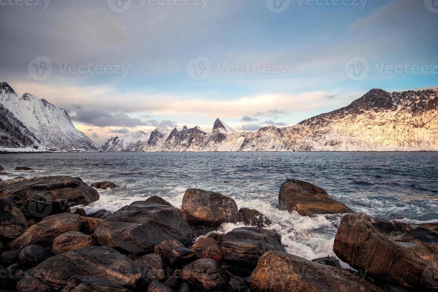 cordilheira de neve e onda batendo no litoral no inverno na ilha de senja foto