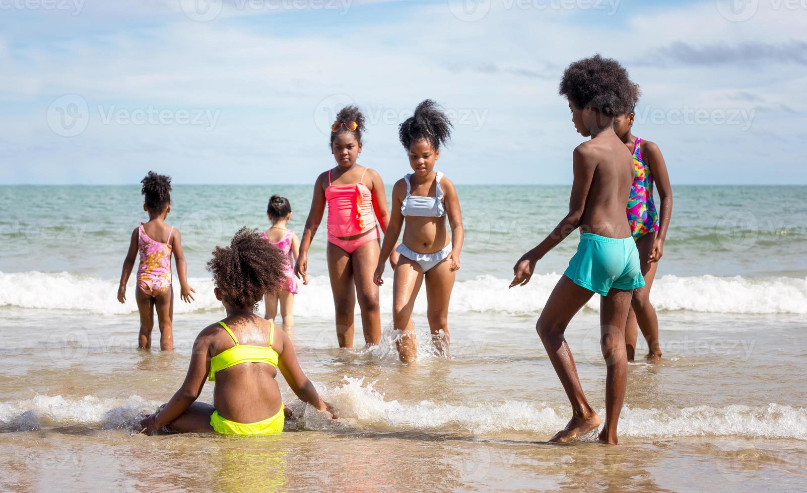 crianças brincando correndo na areia na praia, um grupo de crianças de mãos dadas na praia no verão, vista traseira contra o mar e o céu azul foto