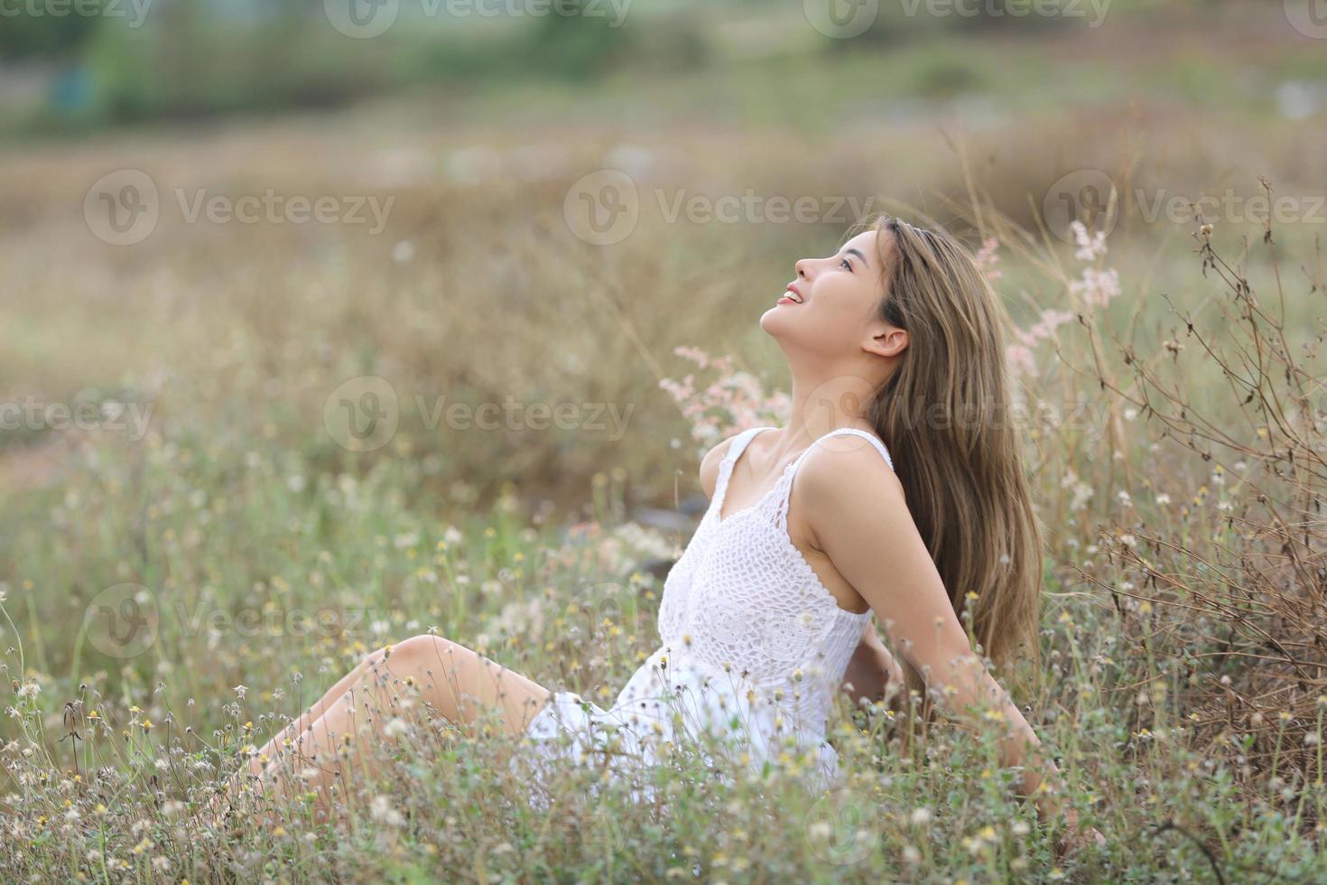 bela jovem sentada no campo na grama verde e soprando dente de leão. ao ar livre. Aproveite a natureza. menina sorridente saudável no gramado da primavera. conceito livre de alergia. liberdade foto