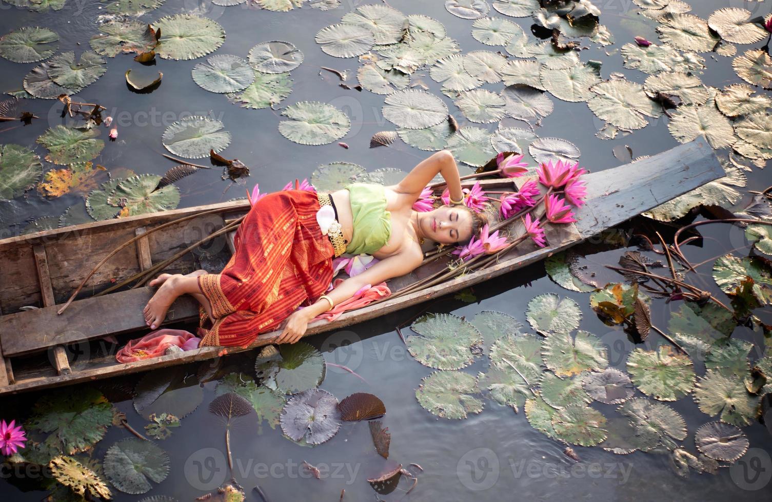 jovens mulheres asiáticas em trajes tradicionais no barco e flores de lótus rosa na lagoa foto