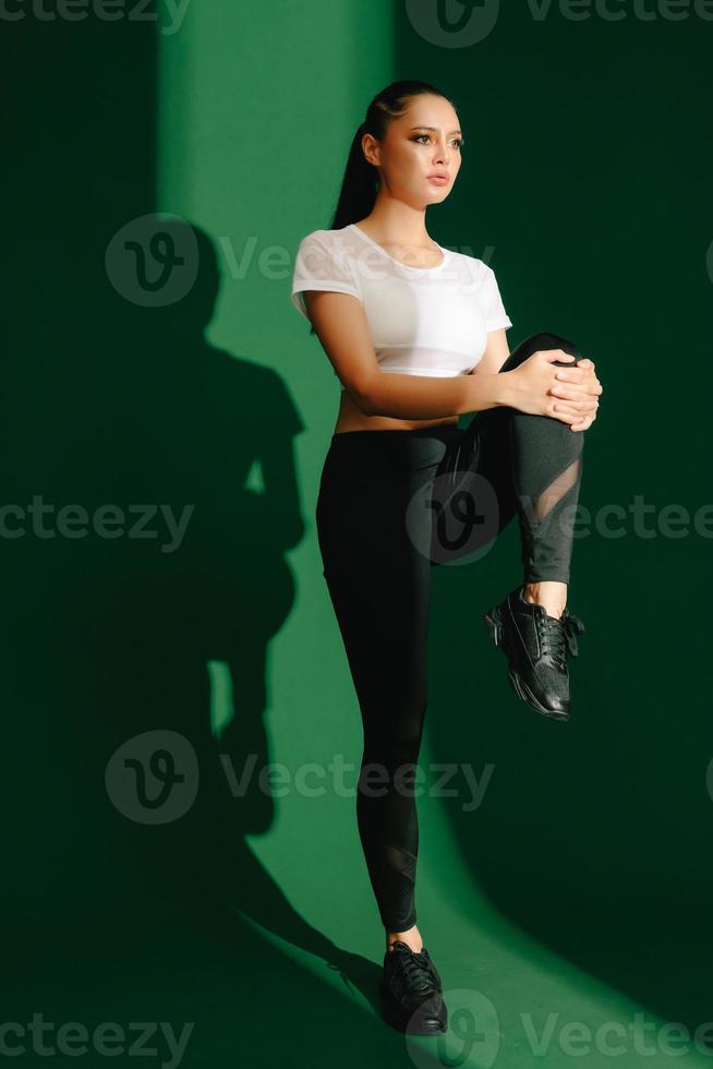 bela forte feliz alegre jovem mulher de esportes asiáticos faz exercícios isolados sobre fundo verde. garota fitness em roupas esportivas posando dentro de casa. movimento, força e motivação. foto