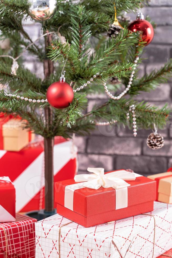 árvore de natal decorada com lindos presentes vermelhos e brancos embrulhados em casa com parede de tijolos pretos, conceito de design festivo, close-up. foto