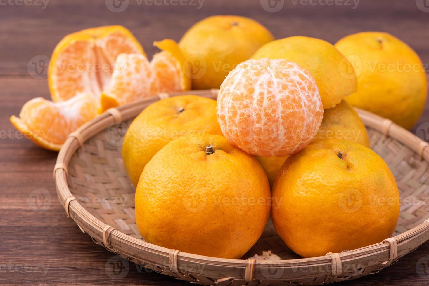 fresca, linda tangerina de cor laranja na peneira de bambu sobre a mesa de madeira escura. fruta sazonal e tradicional do ano novo lunar chinês, close-up. foto