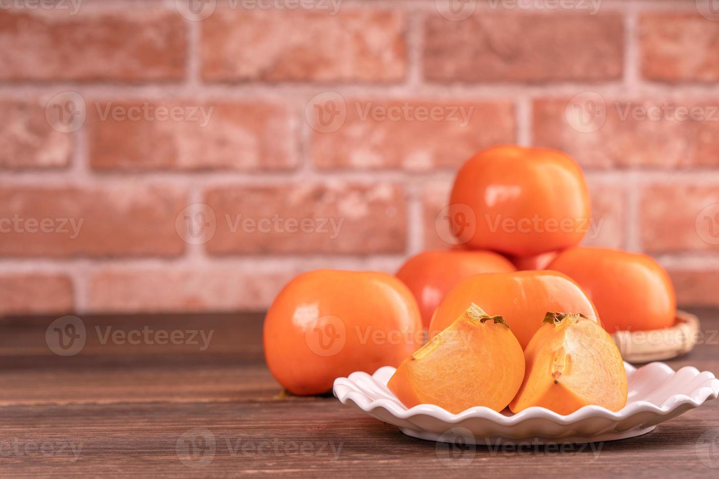 caqui de caqui doce fatiado em uma cesta de peneira de bambu na mesa de madeira escura com fundo de parede de tijolo vermelho, conceito de design de frutas do ano novo lunar chinês, close-up. foto