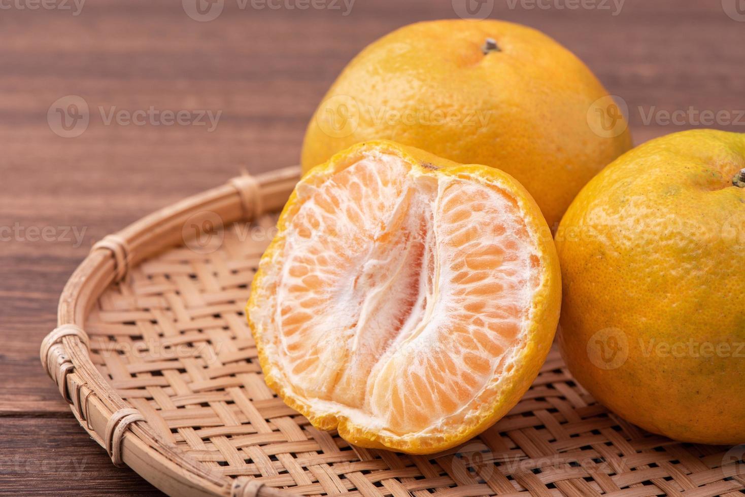 fresca, linda tangerina de cor laranja na peneira de bambu sobre a mesa de madeira escura. fruta sazonal e tradicional do ano novo lunar chinês, close-up. foto