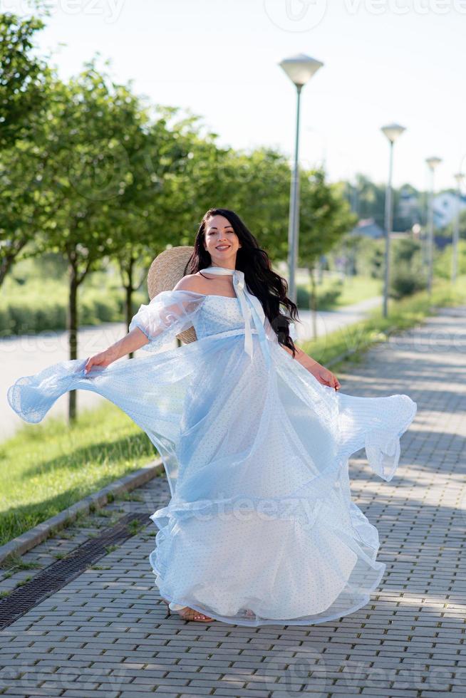 mulher grávida de chapéu posando em um vestido em um fundo de árvores verdes. foto