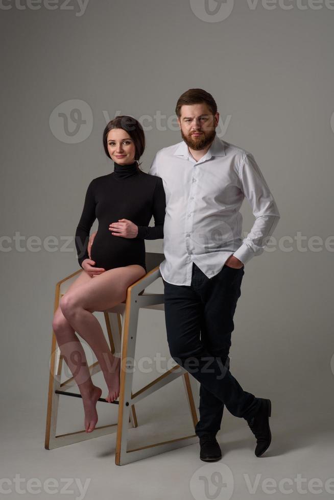 uma mulher grávida e o marido estão se abraçando em um fundo cinza. casal esperando um bebê. foto