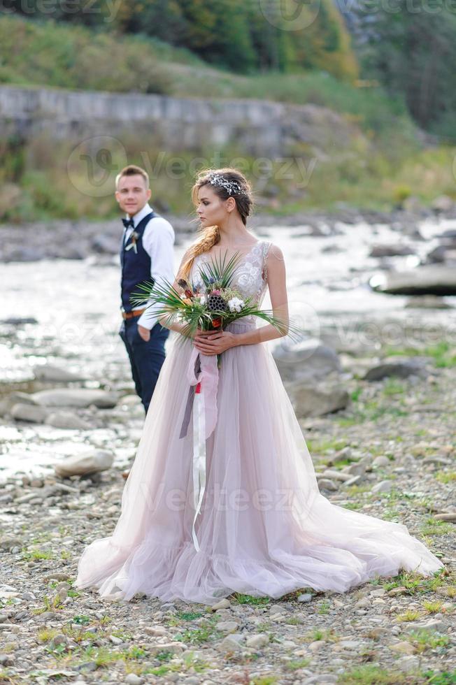 um atraente casal recém-casado, um momento feliz e alegre. um homem e uma mulher se barbeiam e se beijam com roupas de férias. cerimônia de casamento de estilo boêmio na floresta ao ar livre. foto