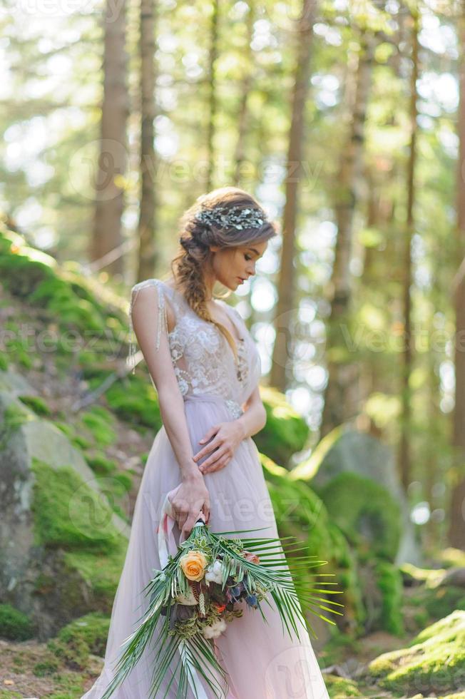 noiva feliz em um vestido de noiva rosa. a garota tem um buquê de casamento nas mãos dela. cerimônia de casamento estilo boho na floresta. foto