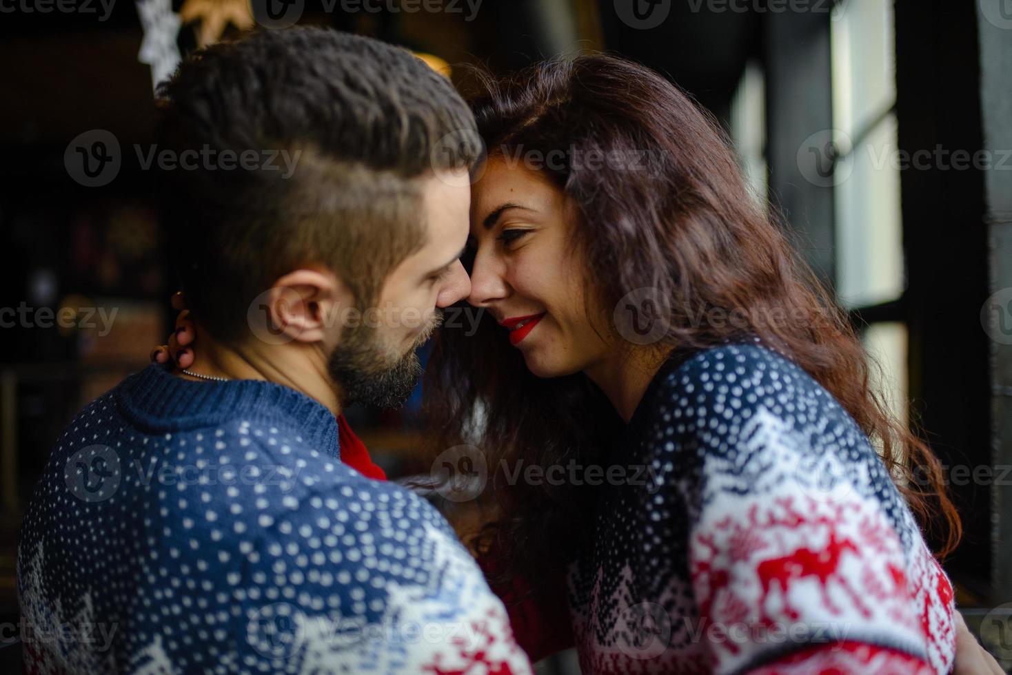 jovem casal apaixonado vestido de suéter azul sentado com xícaras de café de malha no café no inverno foto