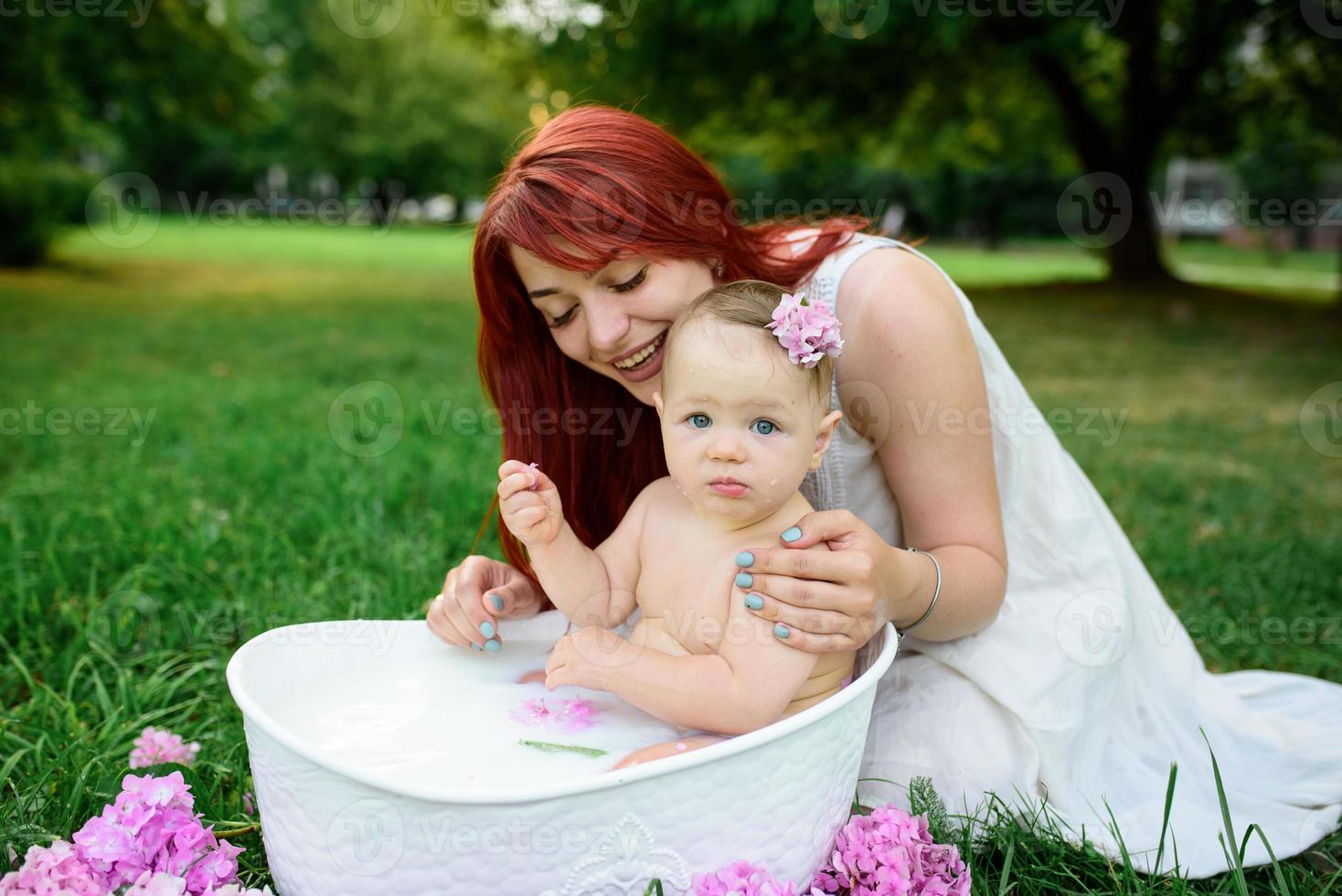 mãe ajuda sua filhinha de um ano a tomar banho no banheiro. filmado em um parque ao ar livre na natureza. foto
