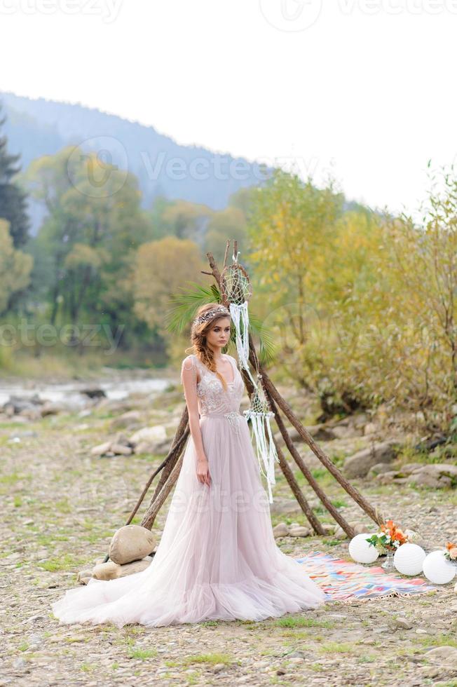 noiva feliz em um vestido de noiva rosa. a garota tem um buquê de casamento nas mãos dela. cerimônia de casamento estilo boho na floresta. foto