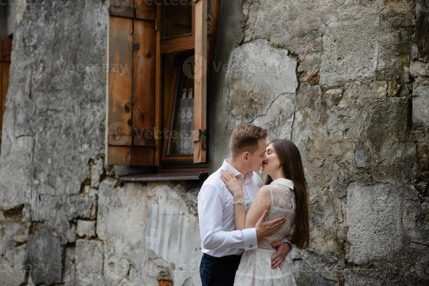 casal apaixonado está beijando e abraçando sobre o muro urbano cinza na cidade de manhã. homem e mulher estão se divertindo muito juntos. antiga antiga rua da cidade europeia com paredes de pedra. foto