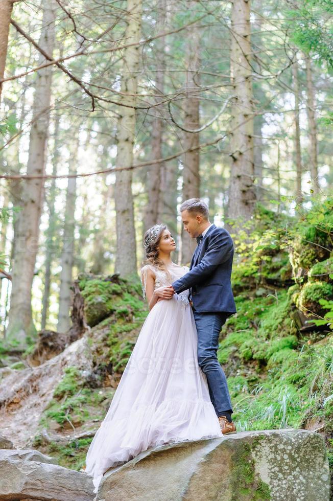 um atraente casal recém-casado, um momento feliz e alegre. um homem e uma mulher se barbeiam e se beijam com roupas de férias. cerimônia de casamento de estilo boêmio na floresta ao ar livre. foto